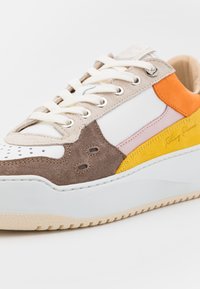 Sneaker med en blandning av vit läder, brun och grå mocka, accentuerad med orange, rosa och gula lappar. Strukturerad sula och kurvad design.