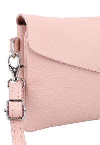 Šviesiai rožinė tekstūra turinti odinė per petį nešiojama rankinė su sidabriniu sukimąsi užsegimu ir reguliuojamu dirželio sagtimi ant balto fono.