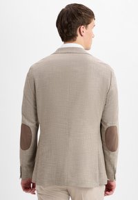 Männlicher sandfarbener Blazer mit strukturiertem Gewebe, braunen Ellenbogen-Patches und zwei Knöpfen an den Manschetten. Strukturierte Passform und klassische Revers.