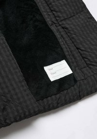 Černá prošívaná látka s měkkým, načechraným interiérem. Obsahuje bílou nálepku pro osobní informace se třemi řádky. Texturovaná a vzorovaná.