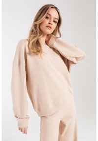 Jasno beżowy sweter z miękkiego materiału o luźnym kroju, okrągłym dekolcie i ściągaczach na mankietach. Posiada opadające ramiona dla większego komfortu.