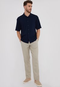 Marineblaues Kurzarm-Hemd mit Knöpfen und subtiler gestreifter Textur, kombiniert mit hellbeigen Hosen und beigen Slippers.