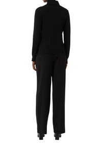 Un pull à col roulé noir en maille douce, associé à un pantalon noir à jambes larges et des chaussures à talons carrés, vu de dos.