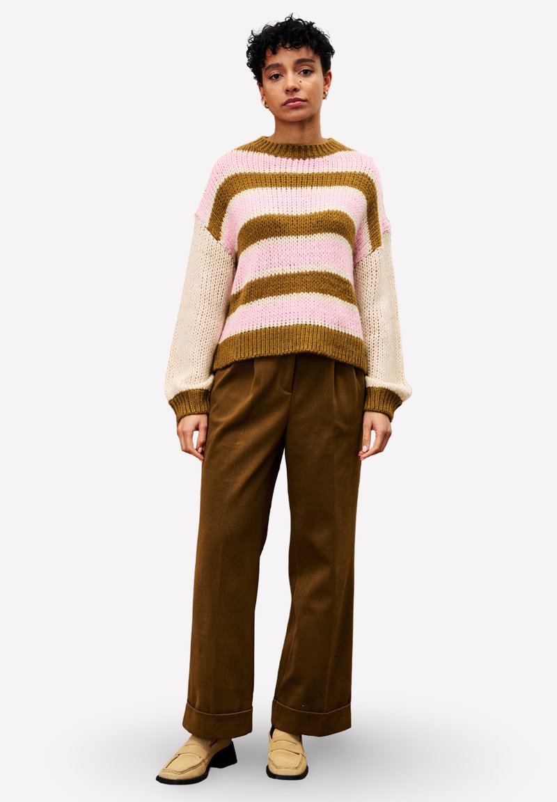 Strickpullover mit pinken, braunen und cremefarbenen Streifen sowie weiten Ärmeln; kombiniert mit braunen weiten Hosen und beigen Slippern.