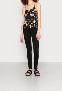Top peplum nero a fiori con spalline sottili, caratterizzato da una vita aderente e un orlo svasato. Abbinato a jeans skinny neri e sandali neri con cinturini.