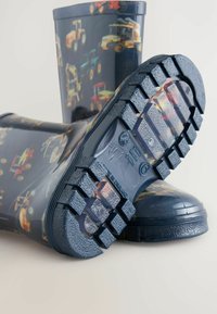 Bottes de pluie bleues en caoutchouc avec une finition brillante. Présentent un motif coloré de tracteurs, des semelles texturées et des crampons profonds pour une meilleure adhérence.