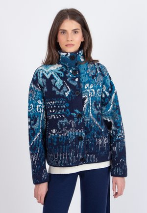 Gebreide jas met een geometrisch patroon in schakeringen van blauw en wit, versierd met zwarte knopen, een hoge kraag en een losse pasvorm.