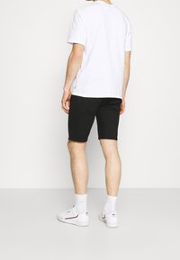 Camiseta blanca de algodón con mangas cortas, combinada con pantalones cortos negros. El modelo lleva zapatillas blancas y calcetines blancos hasta el tobillo.