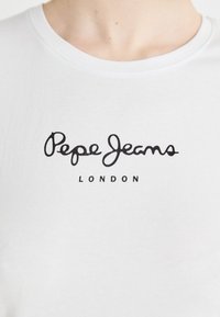 T-shirt en coton blanc avec un logo "Pepe Jeans" en cursif noir et "LONDON" en police gras en dessous du logo. Encolure ronde. Texture plate.