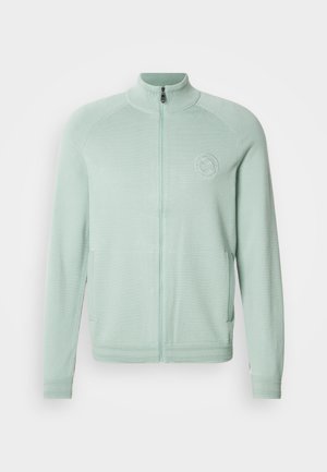 Světlý zelený zipový kabát z měkkého materiálu s vysokým límcem, bočními kapsami a kulatým logem na levé straně hrudi.