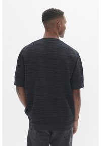 Top tricot scurt cu maneci scurte, de culoare neagră, cu un fit lejer și guler rotund, prezentând modele orizontale subtile. Vedere din spate.
