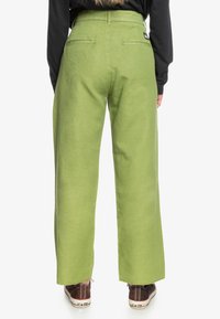 Gröna vida byxor i bomull, med bakfickor och en avslappnad passform. Bärs med bruna sneakers, vilket visar en avslappnad stil.