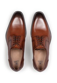 Een paar gepolijste bruine leren nette schoenen met zwarte veters, puntige neuzen en beige binnenzolen op een witte achtergrond.