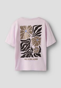 Jasnoróżowa bawełniana koszulka z czarną i złotą grafiką kwiatową z tyłu, z napisem "GRACE IN FULL BLOOM" wydrukowanym poniżej.