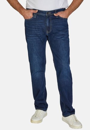Dunkelblaue Jeans im geraden Schnitt, mit Vordertaschen und einem Reißverschluss mit Knopfverschluss. Kombiniert mit weißen Sneakers.