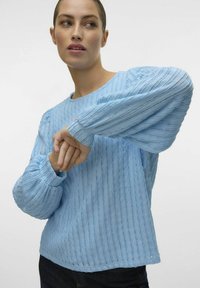 Hele sinine, tekstuuriga pika varrukaga pluus ribakujundusega ja kokku kogutud varrukatega, millel on ümmargune kaelus ja mugav lõige.