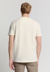 Crème short-sleeve shirt met een geribbelde textuur, ronde halslijn en rechte zoom. Draagt met tan broek, gezien van achteren.