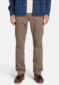 Ruske puuvillased püksid sirge lõikega, koos sinise ruudulise särgiga ja tumedast pruunist nahast kingadega, millel on heledad nööbid ja kare tald.