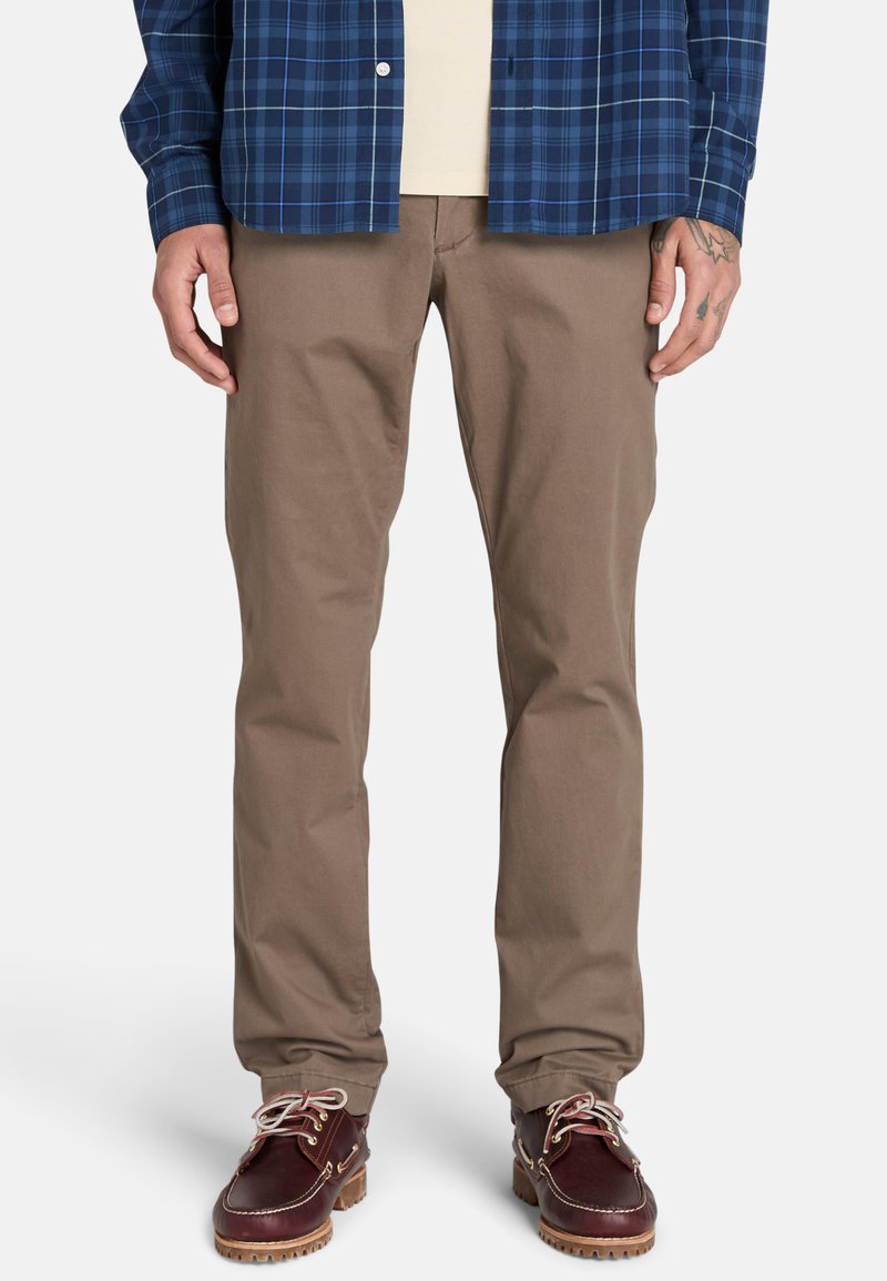 Ruske puuvillased püksid sirge lõikega, koos sinise ruudulise särgiga ja tumedast pruunist nahast kingadega, millel on heledad nööbid ja kare tald.