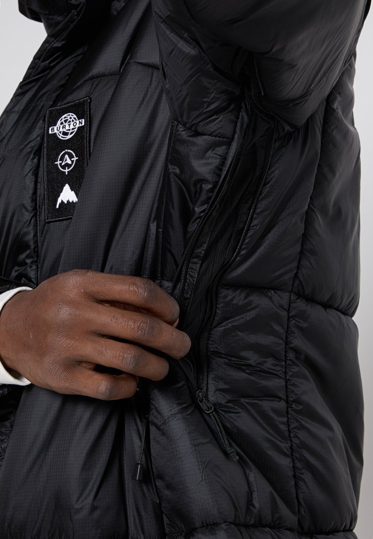 Schwarze Steppjacke mit glatter Textur, ausgestattet mit einer Reißverschlusstasche und einem aufgenähten Logo. Hand, die den Reißverschluss anpasst.