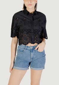 Cropped shirt nera con motivi floreali a intaglio e maniche corte, abbinata a pantaloni corti di jeans a vita alta. Orlo corto e risvolti.
