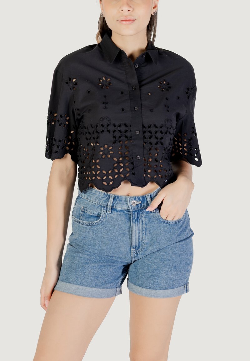 Cropped shirt nera con motivi floreali a intaglio e maniche corte, abbinata a pantaloni corti di jeans a vita alta. Orlo corto e risvolti.