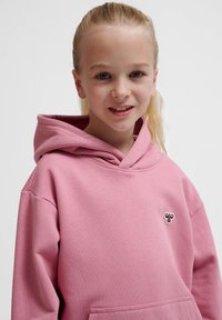 Rosa huvtröja med framficka och broderad logotyp på bröstet. Tillverkad av mjukt material med en avslappnad passform och ribbade manschetter.
