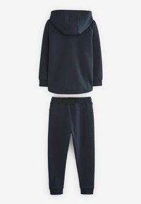 Sweatshirt bleu marine avec capuche et manches longues associé à un pantalon de jogging assorti. Texture lisse, taille élastique et bas de jambes resserrés.