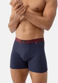 Námořnické modré bavlněné boxerky s vínovým pasem, nabízející přední kapsu a hladkou texturu, navržené pro pohodlí a podporu.