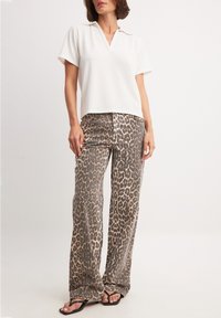 Balta īsām piedurknēm polo krekls ar V-veida kakla izgriezumu, kombinēts ar platām leopardu raksta biksēm, kurās ir brūni un melni toņi. Melni flip-flopi.