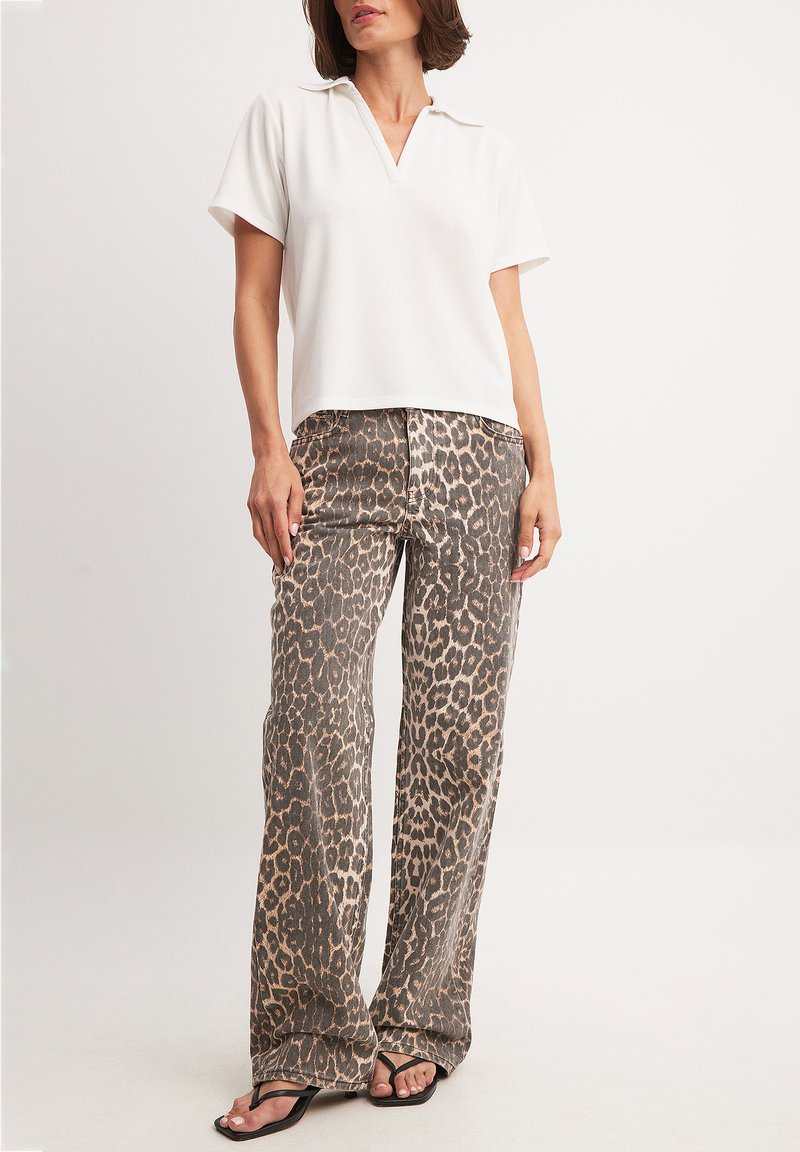 Balta īsām piedurknēm polo krekls ar V-veida kakla izgriezumu, kombinēts ar platām leopardu raksta biksēm, kurās ir brūni un melni toņi. Melni flip-flopi.