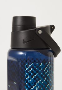 Blå sportsvandflaske med et sort skrue låg og flip-top åbning, tekstureret greb og et bølget design i blå og sort. Nike-logo synligt.