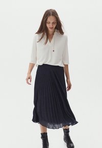 Top bianco a maniche corte con scollatura a V e un accento rosso, abbinato a una lunga gonna a pieghe blu navy e stivali neri alla caviglia.