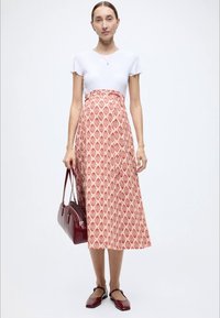 Jupe maxi à motifs rouges avec haut blanc, assortie à un sac à main bordeaux et des chaussures assorties, sur fond neutre.