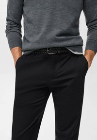 Suéter de punto gris con mangas largas, combinado con pantalones negros de corte recto y un cinturón trenzado negro. Diseño sencillo, sin patrones o decoraciones visibles.