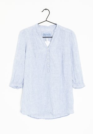 Ljusblå linneblus på en galge, med V-ringning, långa ärmar med uppvikta manschetter och en knappslå med fem knappar.