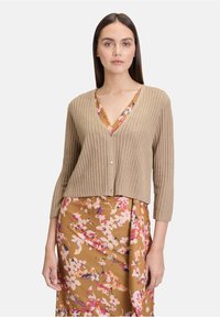 Beige Rippstrick-Cardigan mit V-Ausschnitt und Dreiviertelärmeln, mit Knopfverschluss, über einem blumenmusterhaften Kleid getragen.