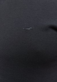 Czarna koszulka polo z teksturowanej tkaniny, z małym, tonalnym logo konia umieszczonym po lewej stronie klatki piersiowej.