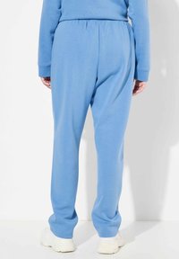 Pantalones de chándal de color azul claro, hechos de material suave, con cintura y puños elásticos. El diseño presenta un ajuste relajado y una textura lisa.