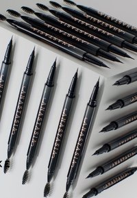 Ensemble de crayons à sourcils noirs avec pointes fines et brosses spoolie, arborant des lettres dorées et un design cylindrique élégant.