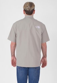 Camicia a maniche corte khaki con yoke posteriore, realizzata in tessuto leggero. Presenta un logo bianco sulla parte superiore della schiena e un fit comodo.