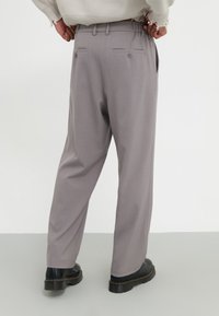Light gray trousers with a straight, relaxed fit, featuring two back pockets with buttons, and paired with black lace-up boots.