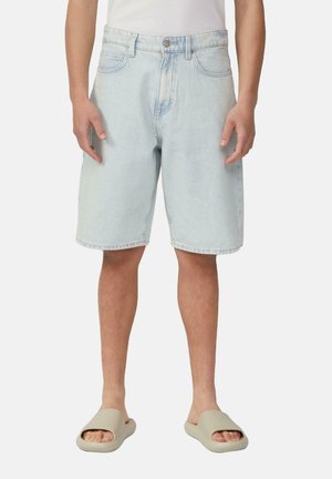 Shorts en denim bleu clair avec une coupe décontractée, comportant des poches avant, une fermeture à bouton et des surpiqûres visibles. Portés avec des sandales à glisser beiges.