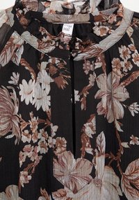 Blouse noire à imprimé floral avec des fleurs marron clair et crème. Elle possède un col froncé et une patte de boutonnage. Fabriquée en tissu léger et texturé.