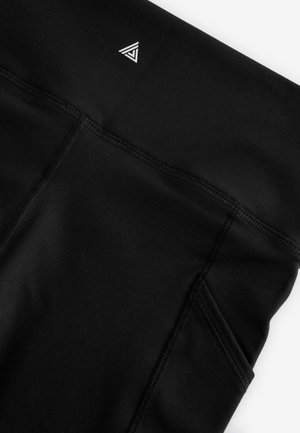 Colanți atletici negri cu o textură netedă, având un logo triunghiular mic și un buzunar lateral. Cusăturile sunt vizibile de-a lungul cusăturilor.