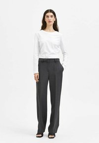 Camicia bianca a maniche lunghe con scollo rotondo, abbinata a pantaloni larghi grigio scuro, sartoriali, con tasche laterali e una trama liscia.
