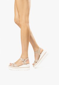 Sandales plateformes beiges avec des brides croisées et une boucle, dotées d'une épaisse semelle blanche et d'une texture en cuir lisse.