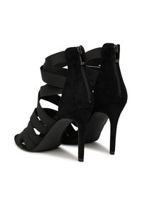 Mustad kõrge kontsaga sandaalid, millel on nahast viimistlus, paelad ja tagumine lukustus. Avatud varvastega stiil tekstureeritud kangast.