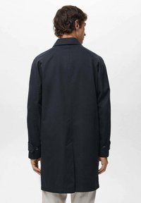 Cappotto blu navy con un design semplice, maniche lunghe, polsini a due bottoni e schiena ventilata, realizzato in un tessuto liscio.