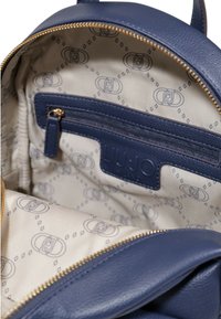 Zaino in pelle blu con zip dorata. L'interno presenta una fodera beige con un motivo logo ripetuto e una tasca con zip per riporre gli oggetti.